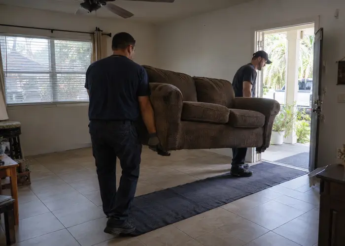 Two people carrying a sofa through a doorway