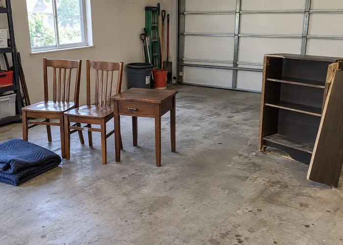 Two wooden chairs, a small table and shelving on a garage floor