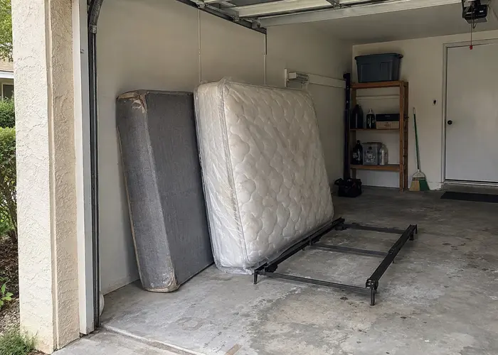 Mattress and box spring beside a metal bed frame in a garage