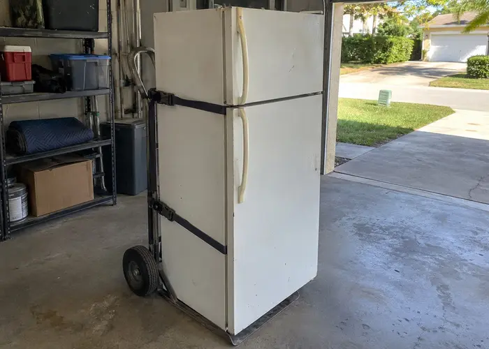 Refrigerator strapped to a hand truck inside an open garage